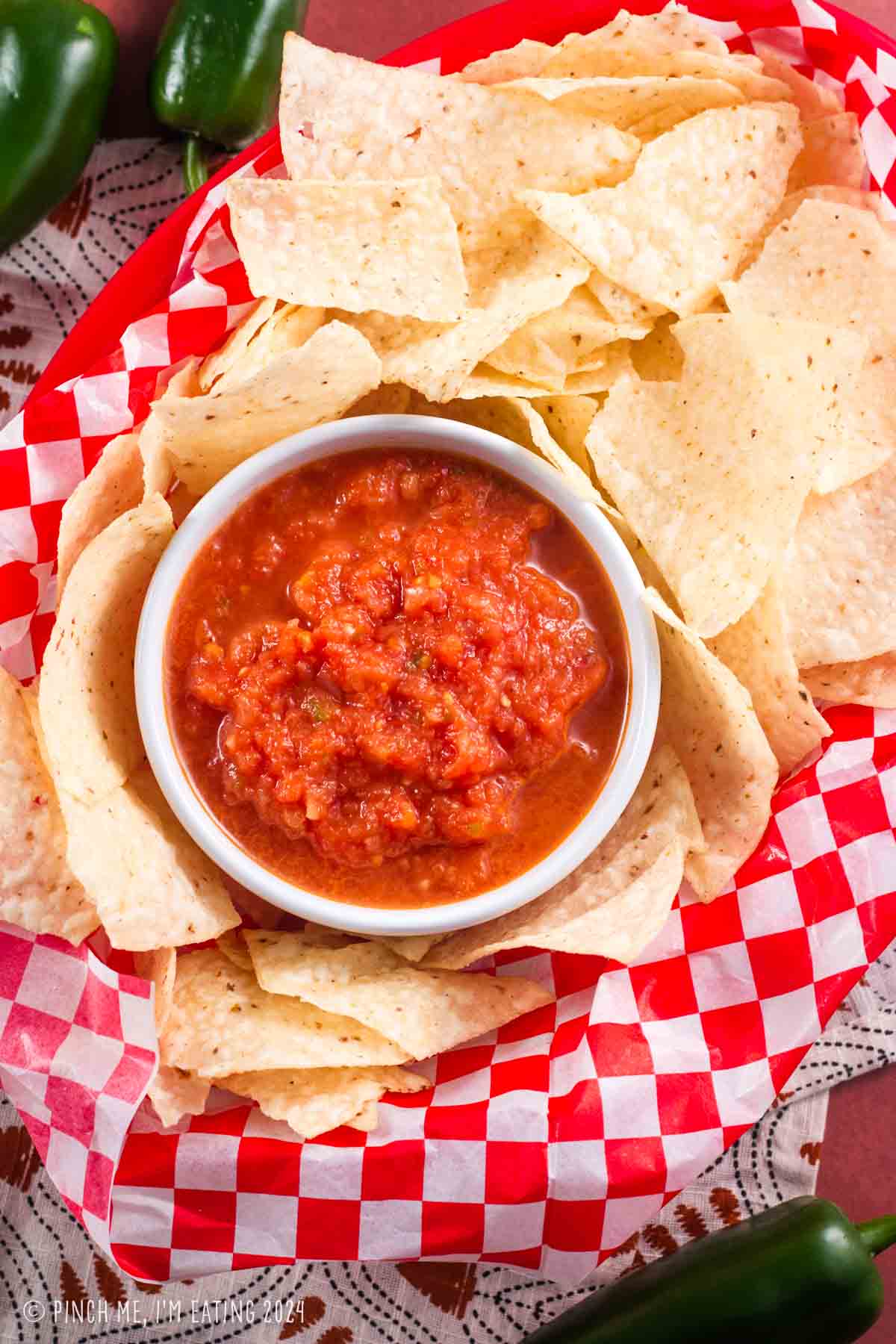 Overhead view of restaurant-style blender salsa in a white bowl surrounded by tortilla chips.