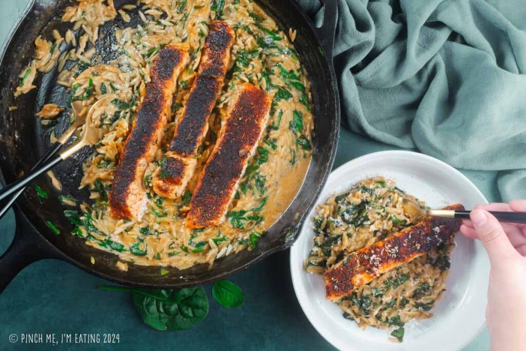 One pan blackened salmon with creamy orzo and spinach in a cast iron skillet.