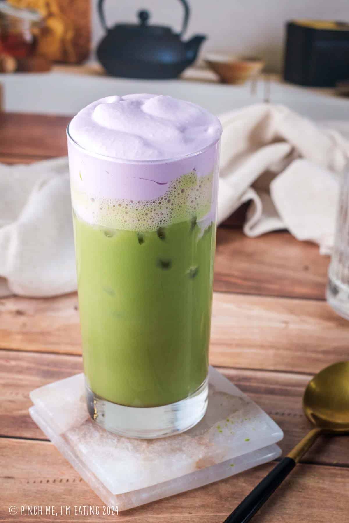Homemade purple and green Starbucks copycat iced lavender cream oatmilk matcha latte in a tall glass next to bottles of simple syrup and lavender syrup.