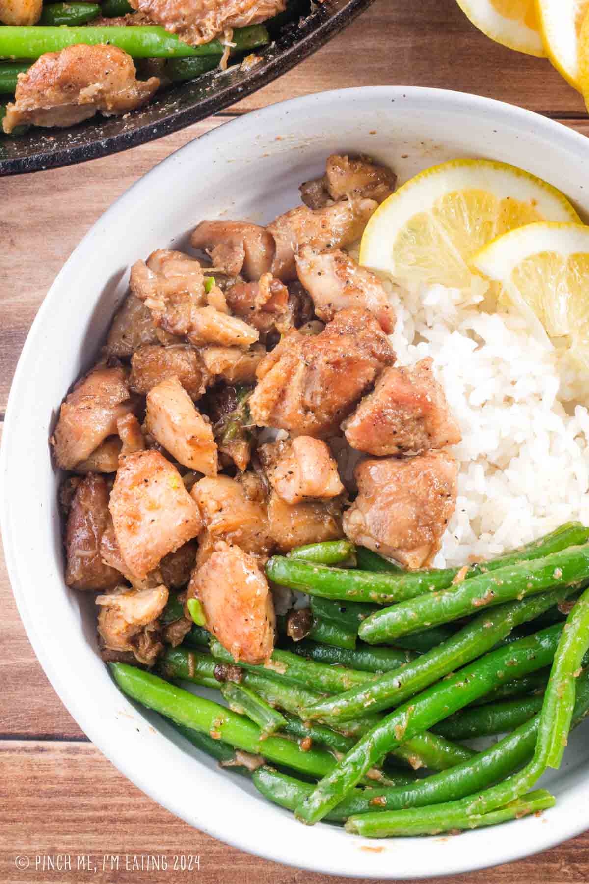 Chicken, rice, and green beans in a white bowl with lemon slices.