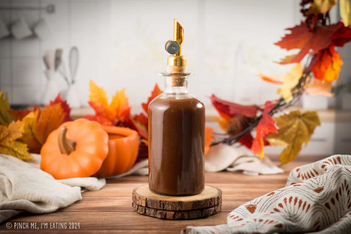 Pumpkin spice sauce in a glass pour bottle with fall decorations. 