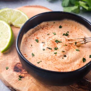Aioli sauce in a black bowl on a wooden board.