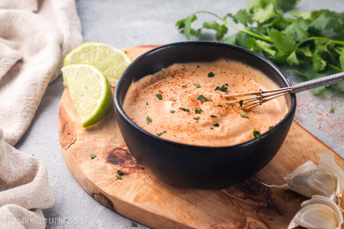 Black bowl of chipotle sauce on a wooden board with lime wedges.