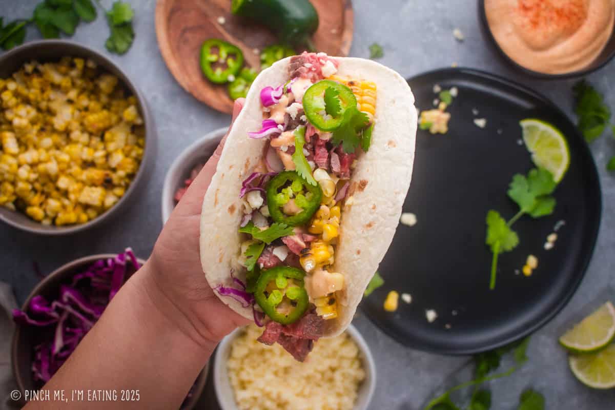 A hand holding a colorful steak and corn taco.