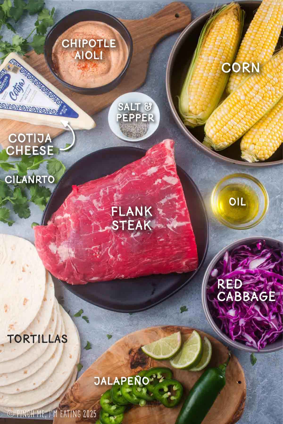 Labeled ingredient shot with flank steak, corn, red cabbage, tortillas, jalapeño pepper, cotija cheese, and chipotle aioli.