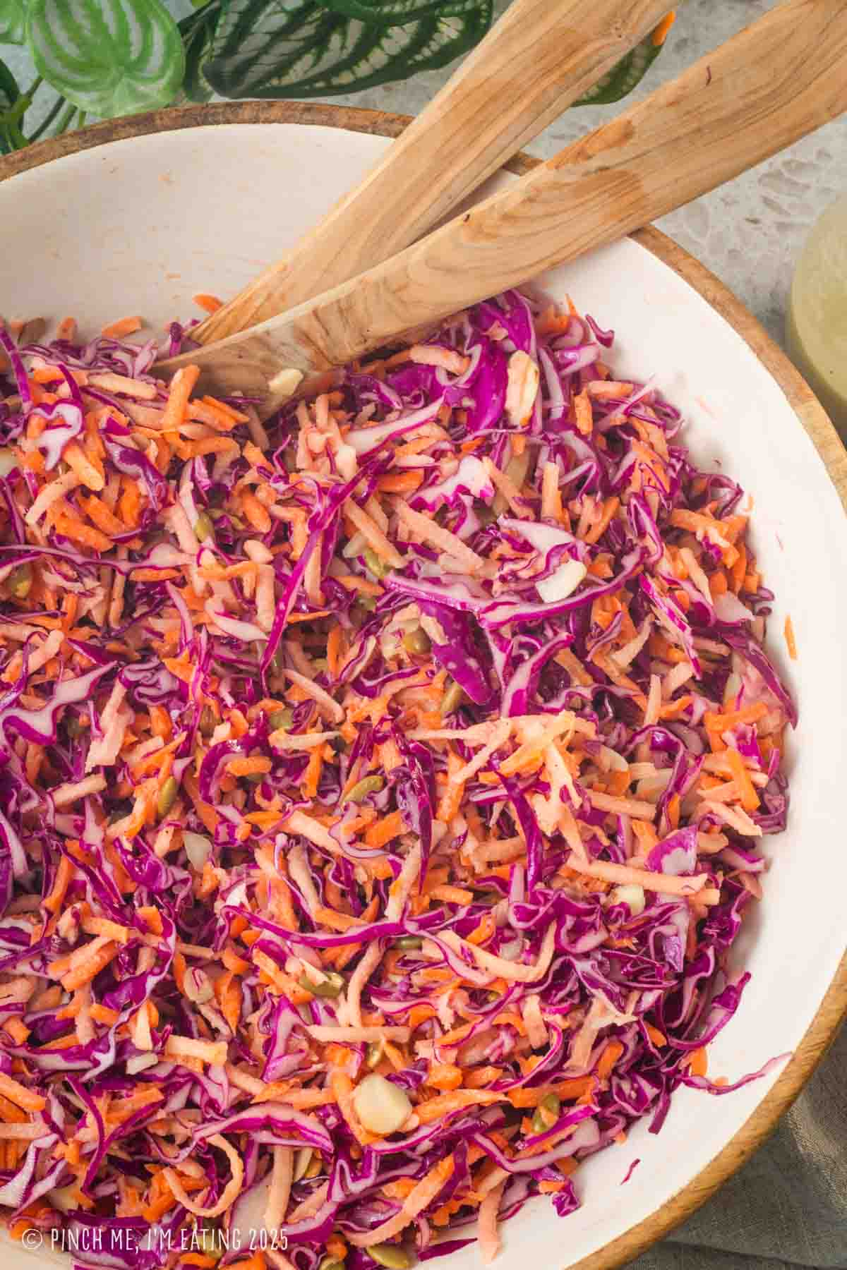 Purple cabbage cole slaw in a large bowl with tongs.