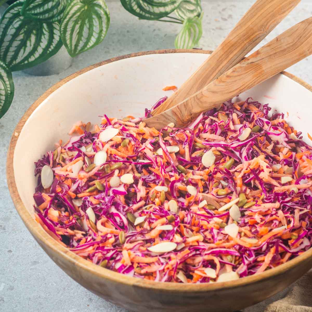 Purple cabbage and carrot slaw in a large bowl with wooden tongs.