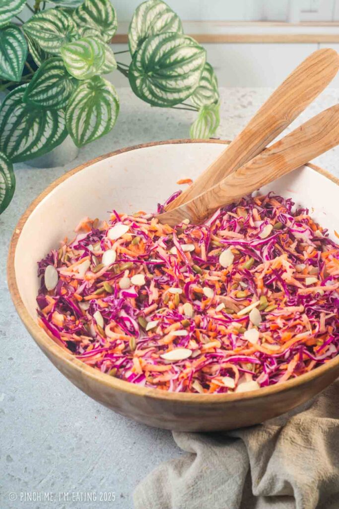 Purple cabbage and carrot slaw in a large bowl with wooden tongs.