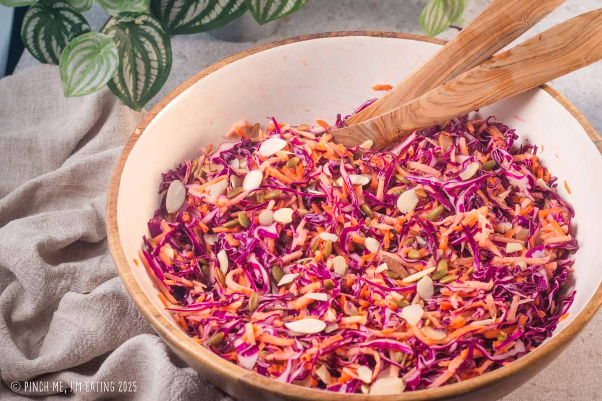 Red cabbage coleslaw in a large bowl with tongs.