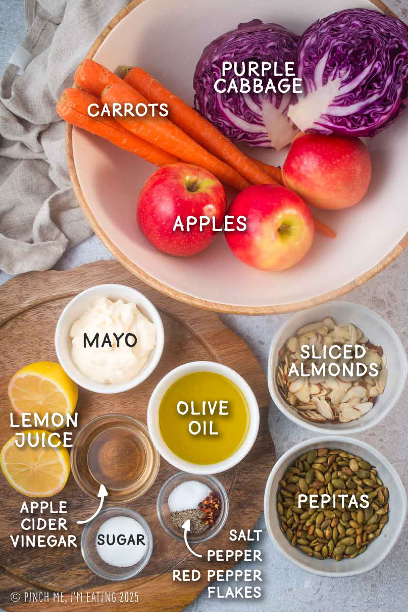 Labeled ingredient shot including purple cabbage, carrots, apples, almonds, pepitas, and ingredients for coleslaw dressing.