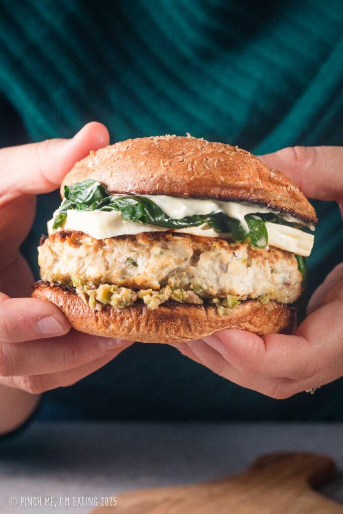 Hands holding a chicken feta burger with sautéed spinach.
