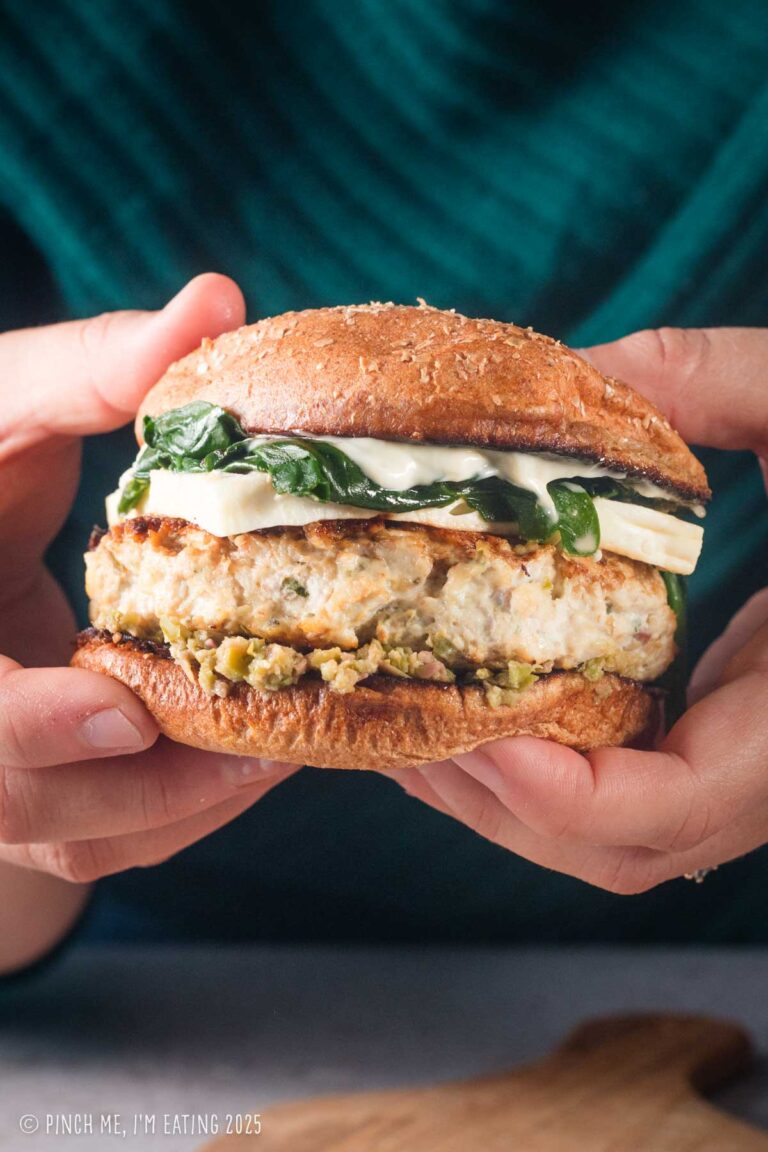 Hands holding a chicken feta burger with sautéed spinach.