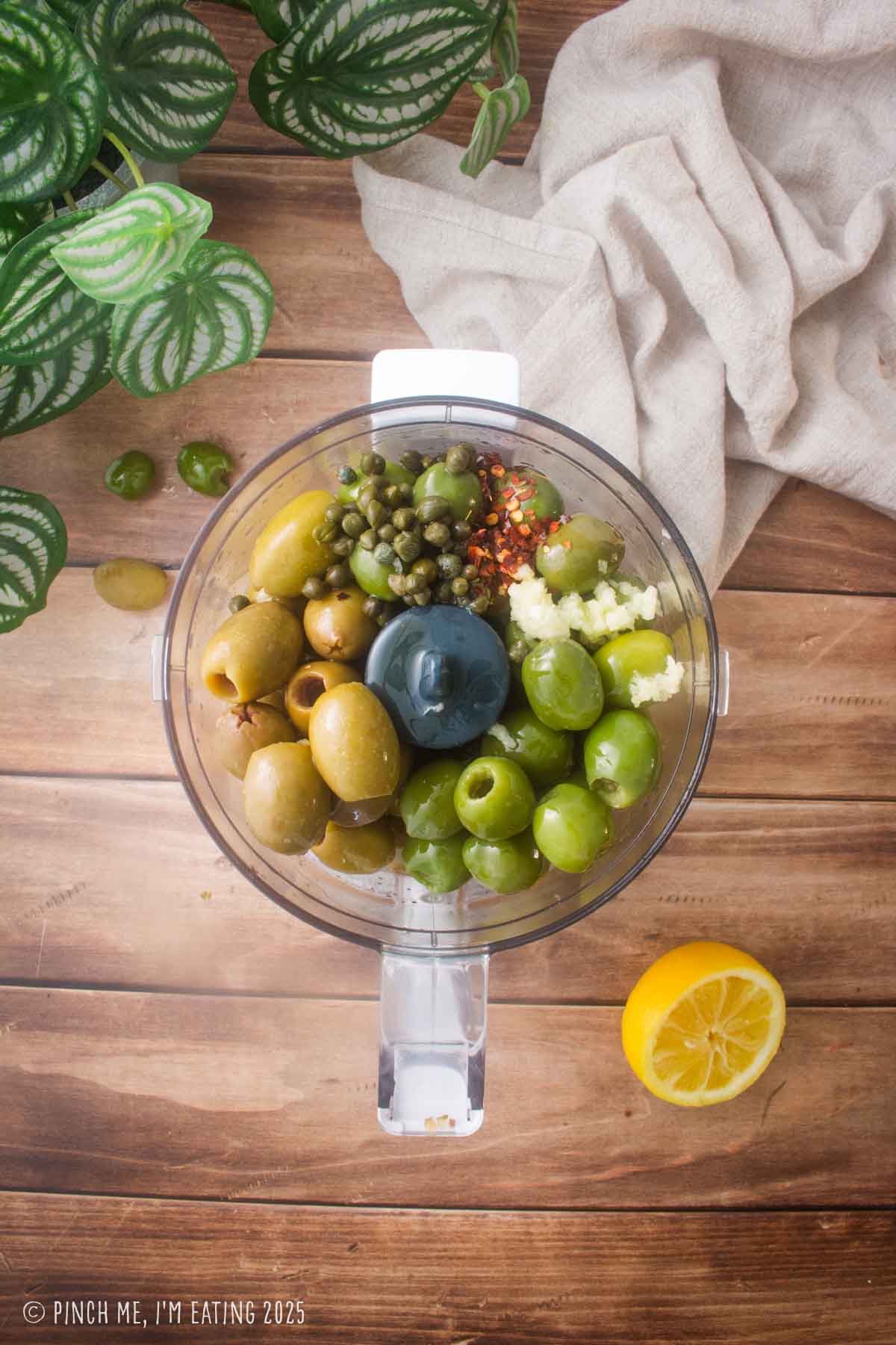Olives, garlic, capers, and other ingredients in a mini food processor.