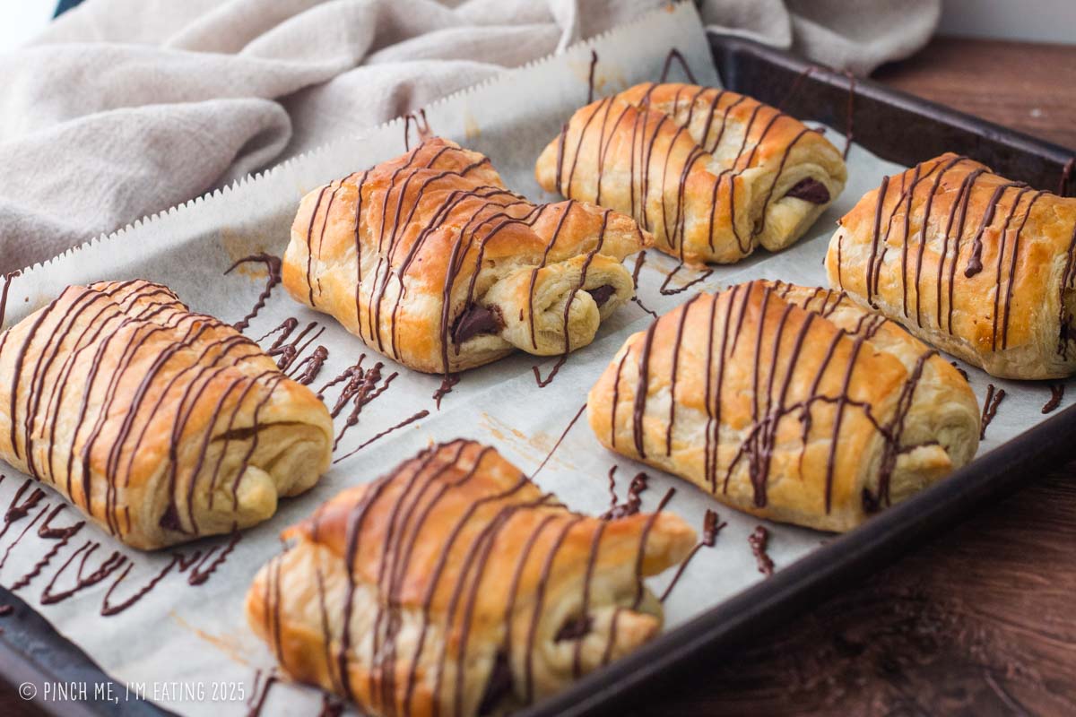 Croissants drizzled with chocolate on a parchment lined baking sheet.