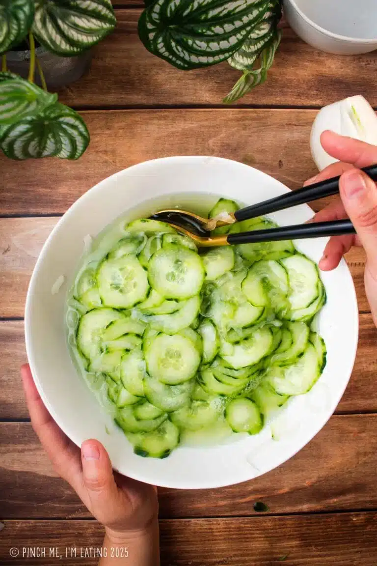 Old fashioned cucumbers and onions in vinegar in a white bowl with serving utensils.