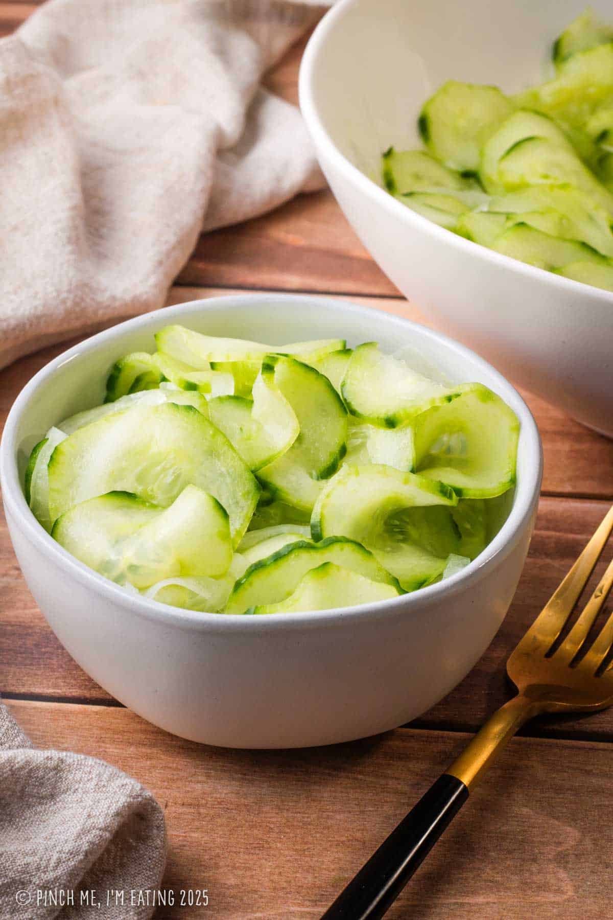 Marinated cucumbers and onions in vinegar in a small white bowl.