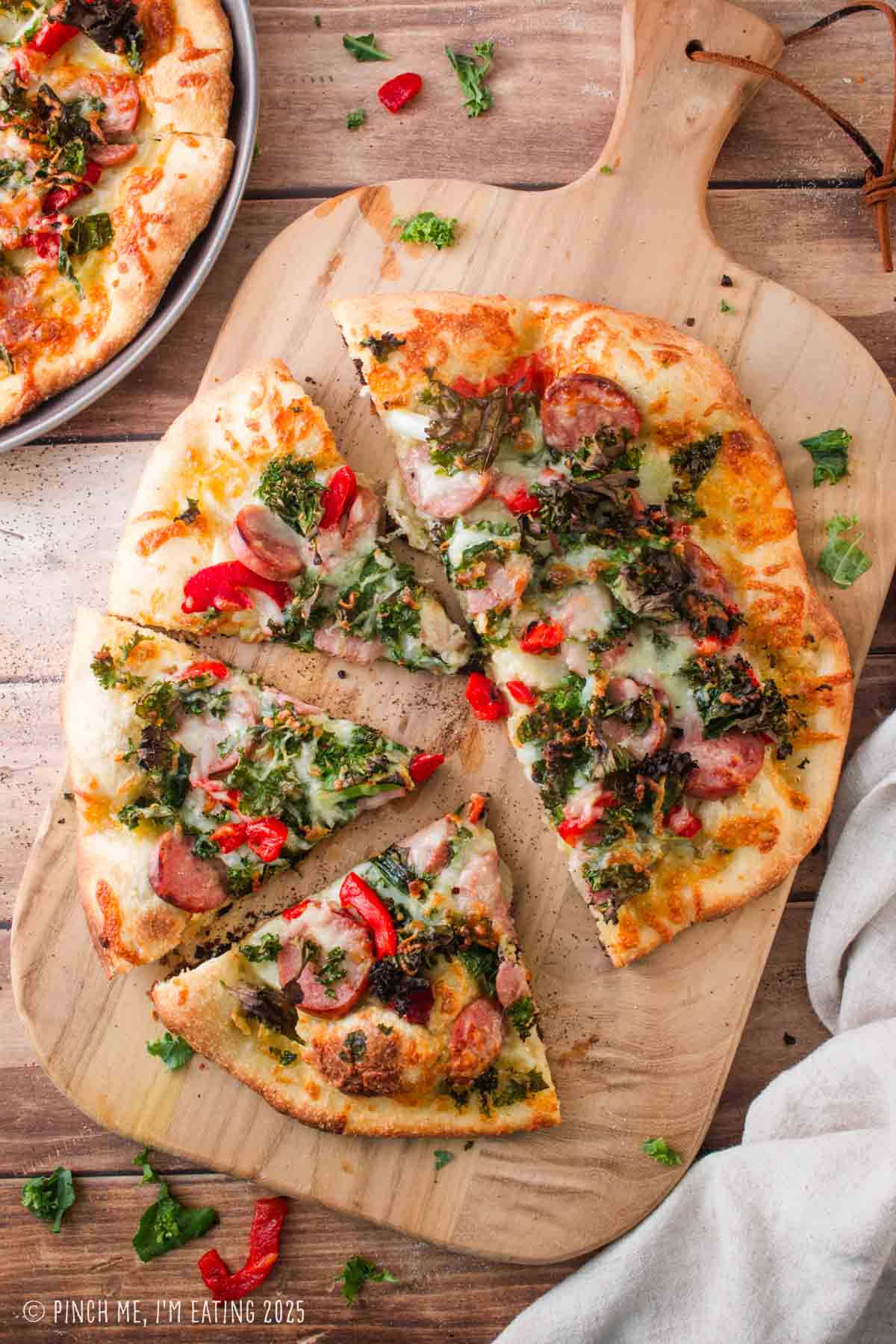 Chicken sausage pizza with kale on a wooden cutting board.