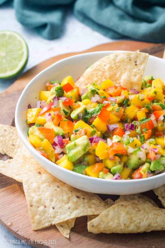 Avocado mango salsa in a white bowl with corn chips.