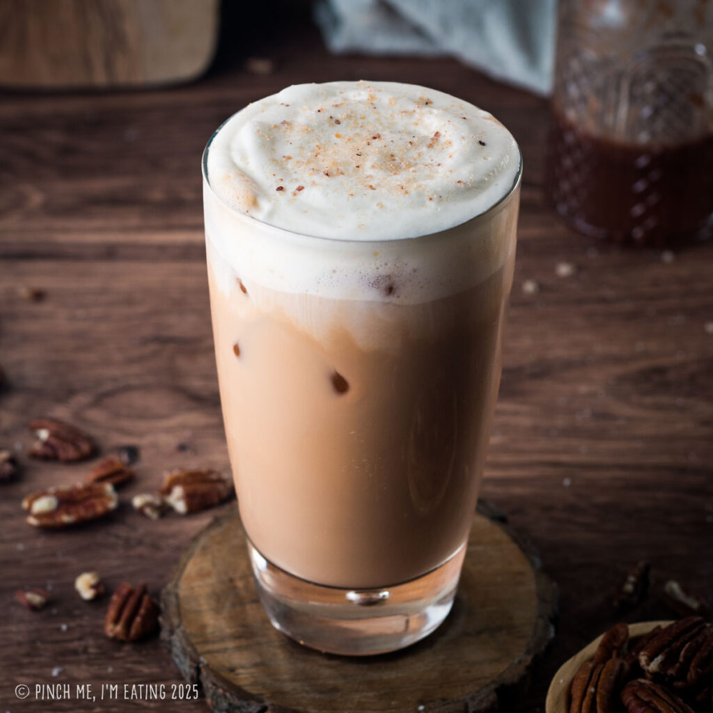 Iced pecan crunch oatmilk latte on a wooden coaster.