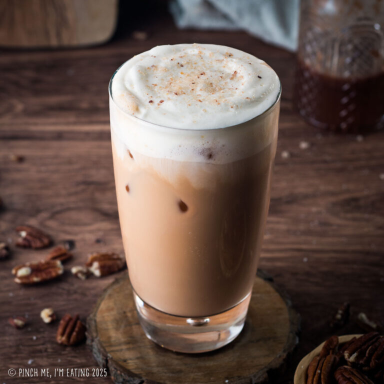 Iced pecan crunch oatmilk latte on a wooden coaster.