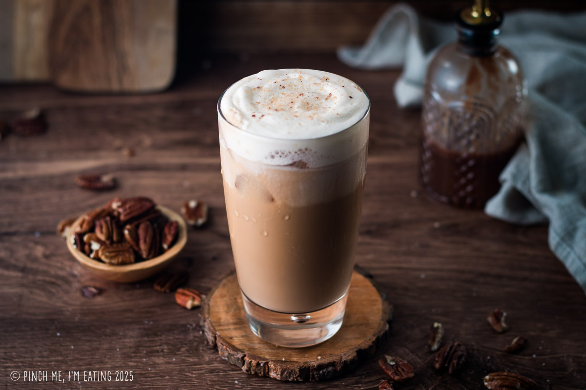 Iced latte with cold foam on a wooden coaster.
