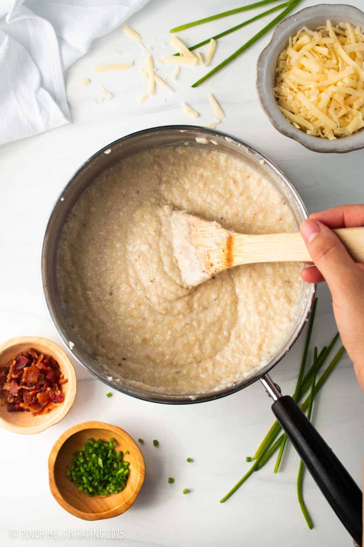 Grits in a pot being stirred with a wooden spoon.