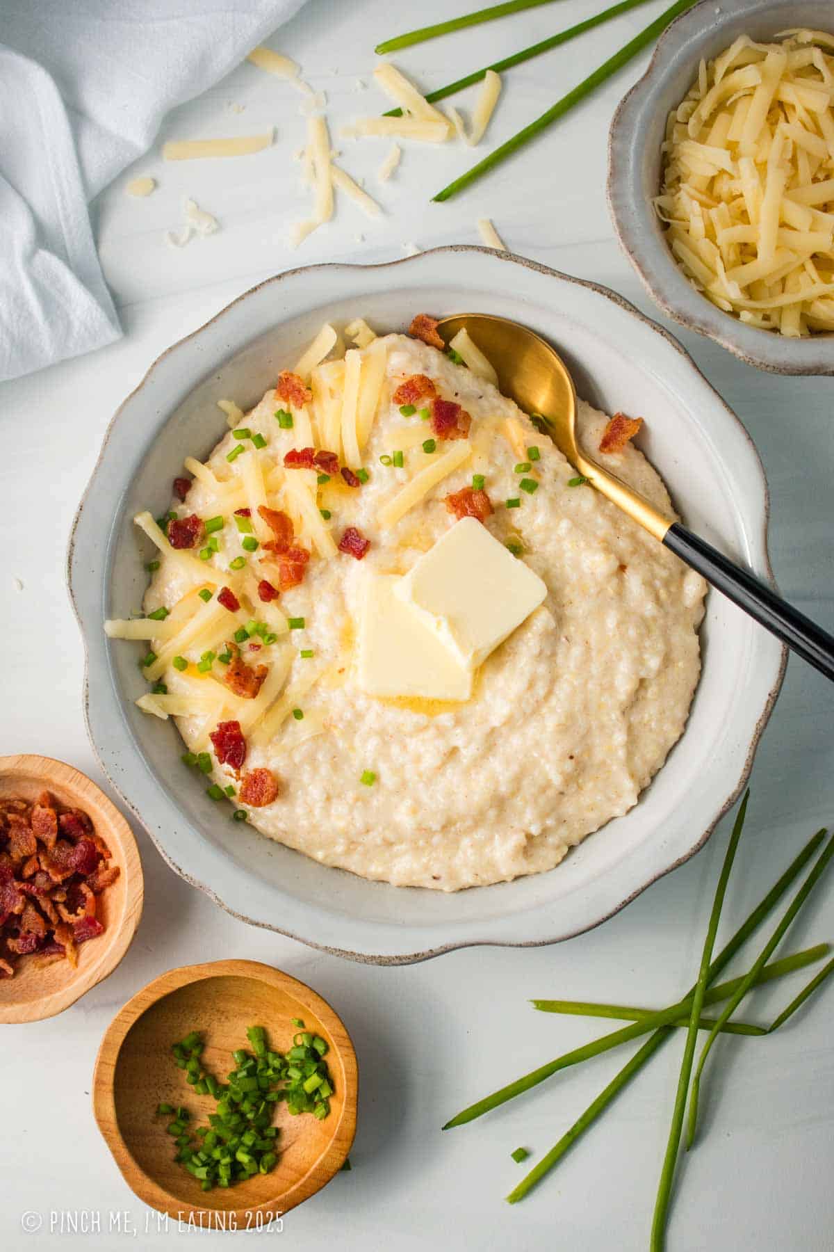 Gouda grits in a white bowl topped with bacon and chives.