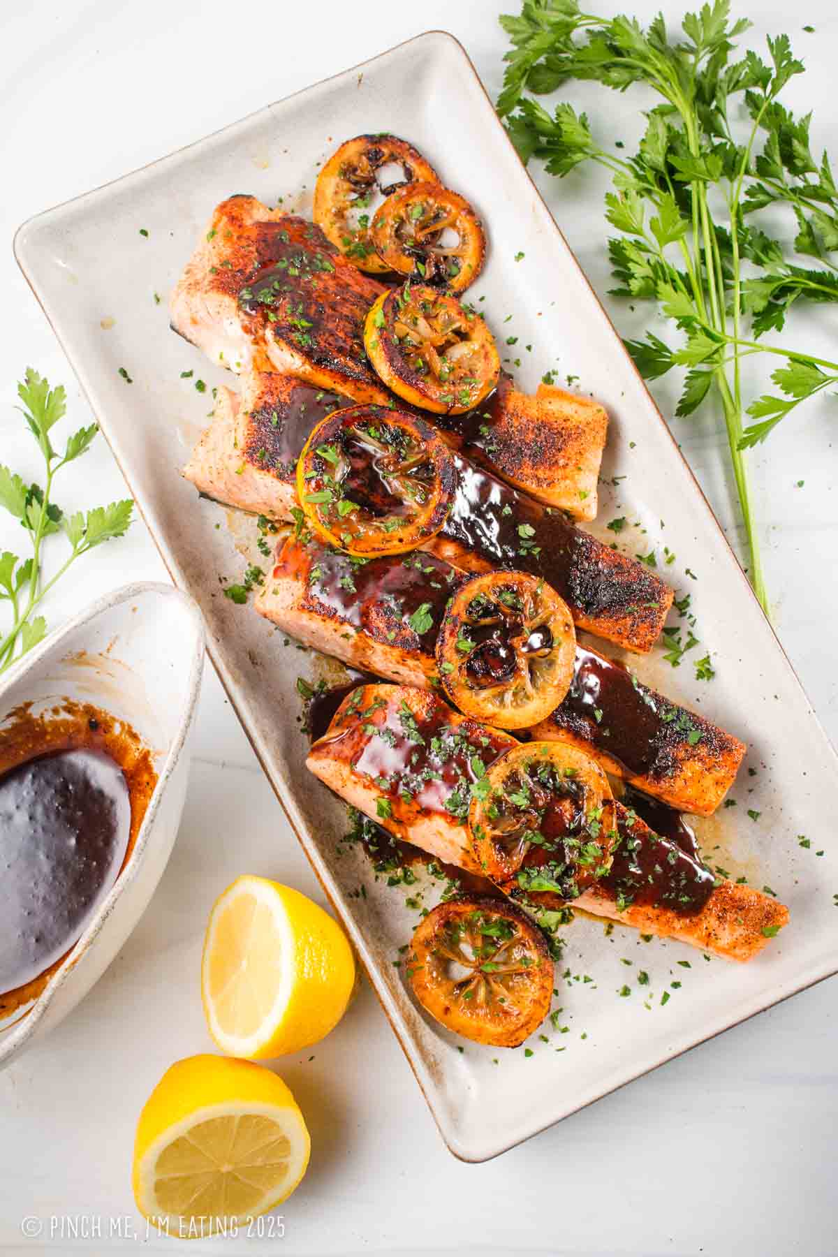 Lemon soy salmon with buttery pan sauce garnished with lemons and parsley on a rectangular serving plate.