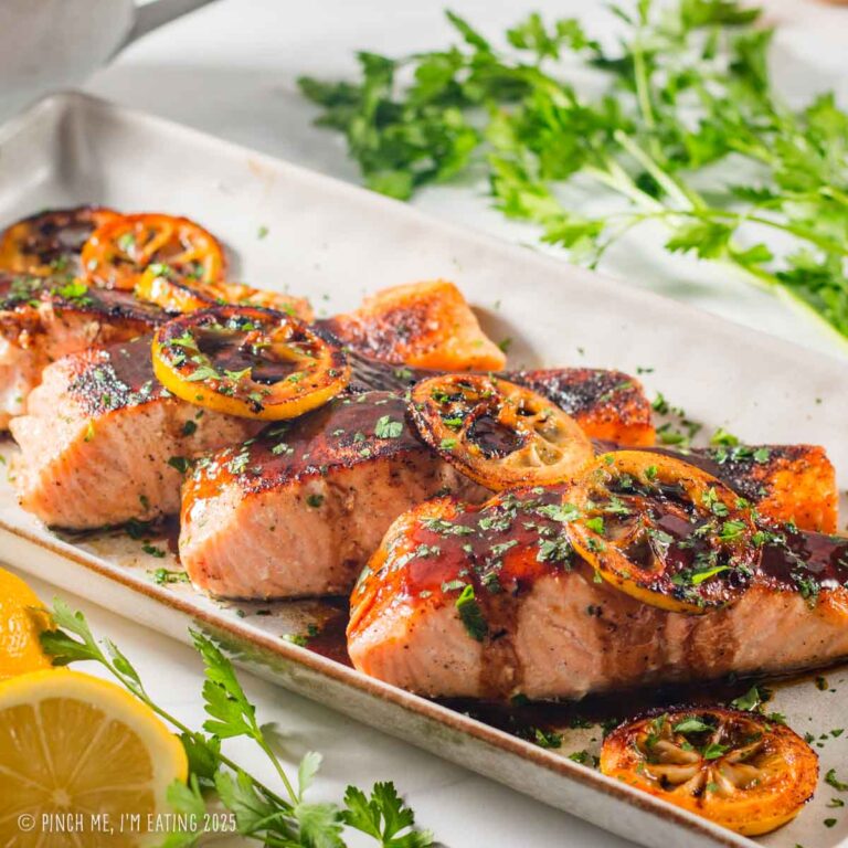 Salmon with soy sauce lemon butter sauce garnished with lemons and parsley on a rectangular serving plate.