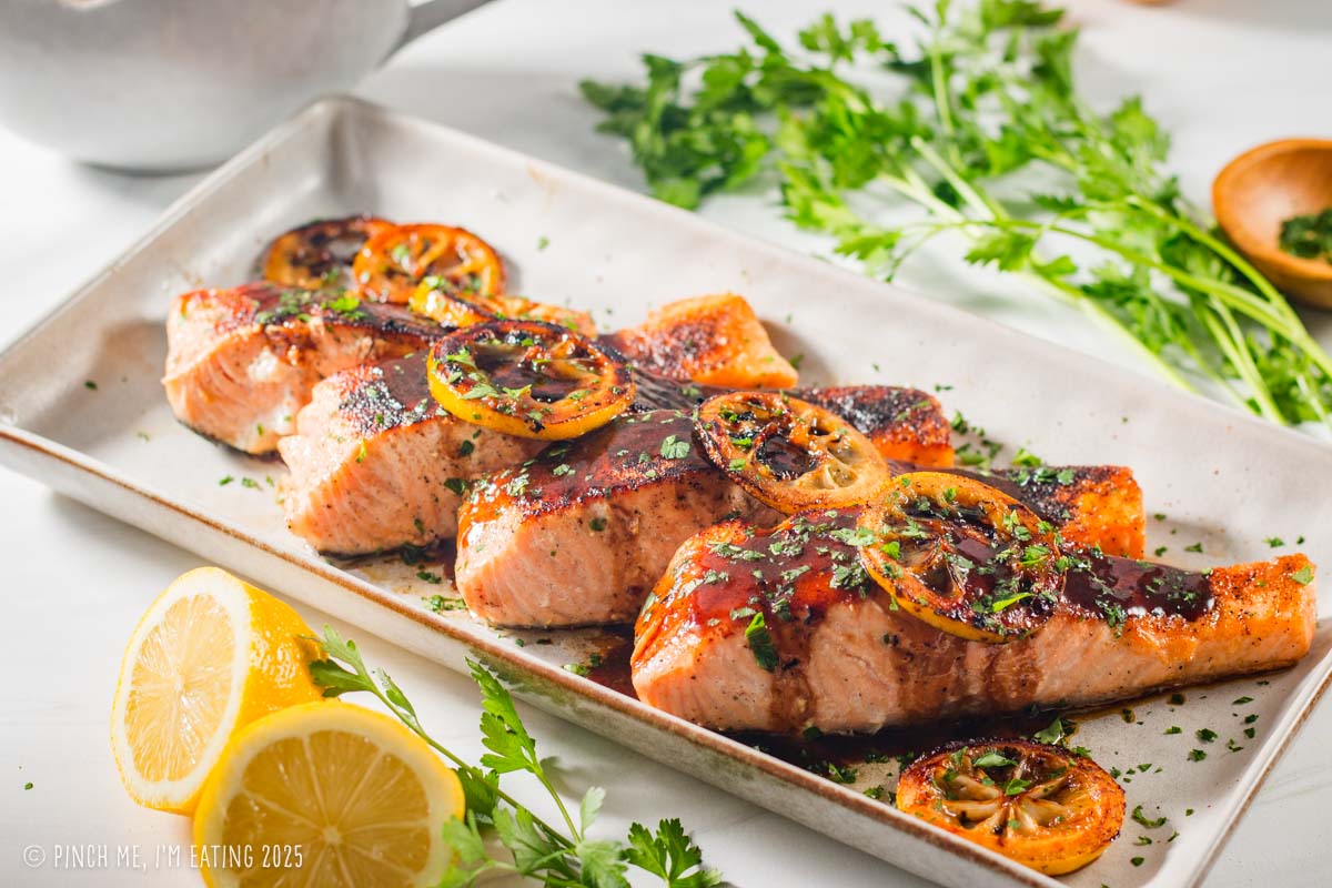 Four pieces of lemon soy salmon garnished with lemon slices and parsley on a rectangular serving plate.