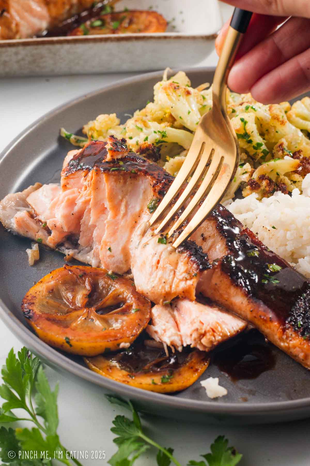 Salmon being flaked apart with a fork, with cauliflower and rice in the background.