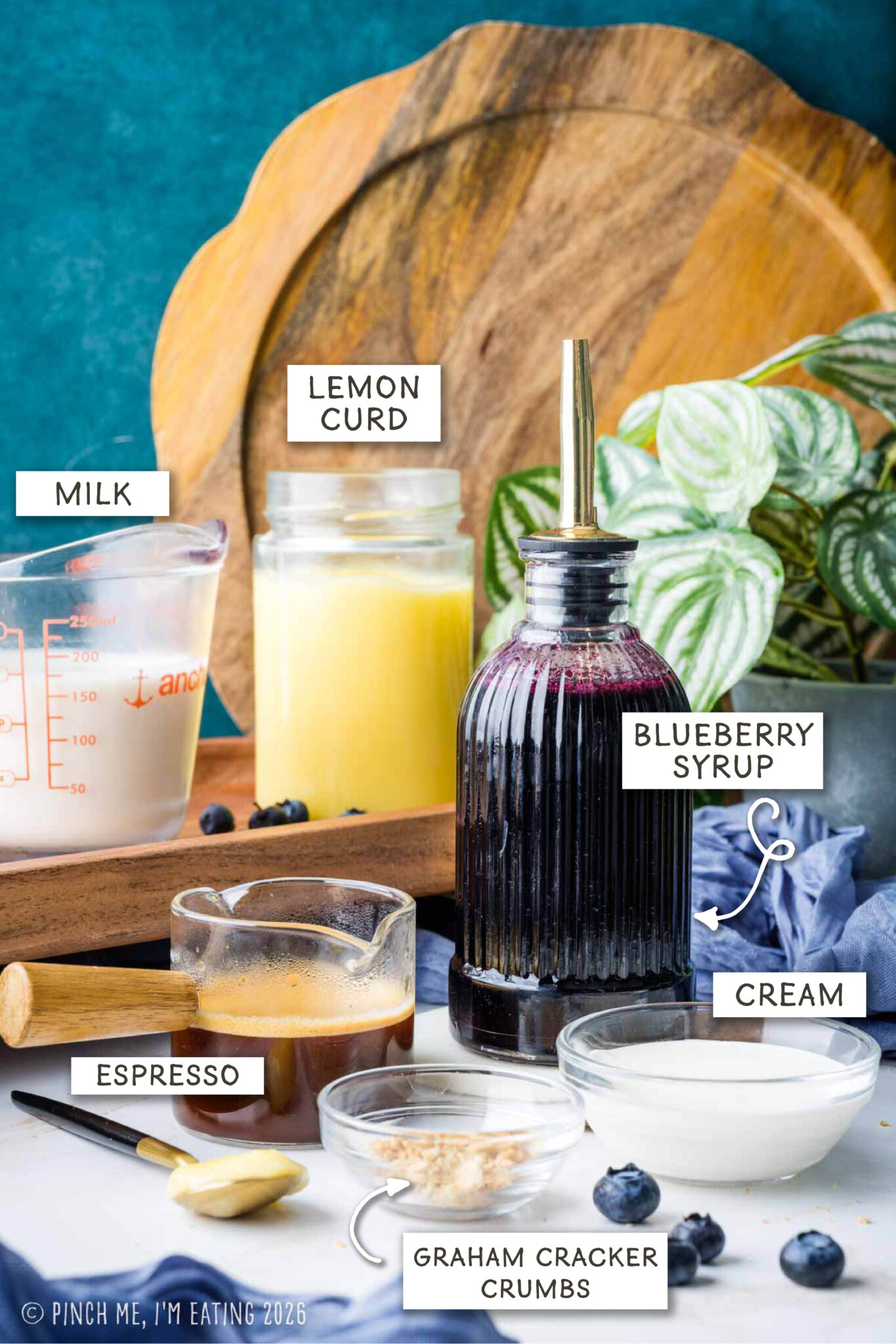A photo of ingredients for a blueberry latte, including espresso, milk, cream, blueberry syrup, lemon curd, and graham cracker crumbs.