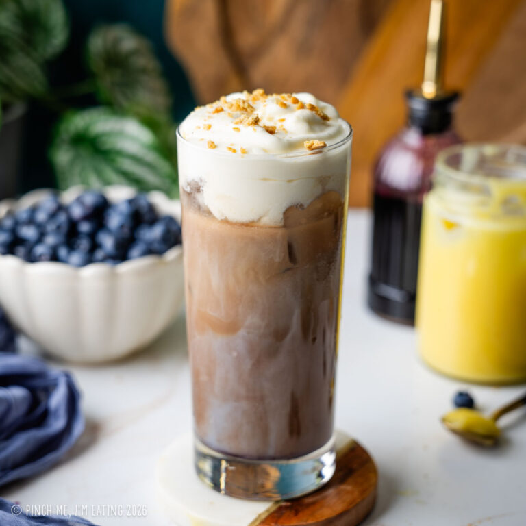An iced blueberry latte topped with lemon curd cold foam and graham cracker crumbs, served in a tall glass.