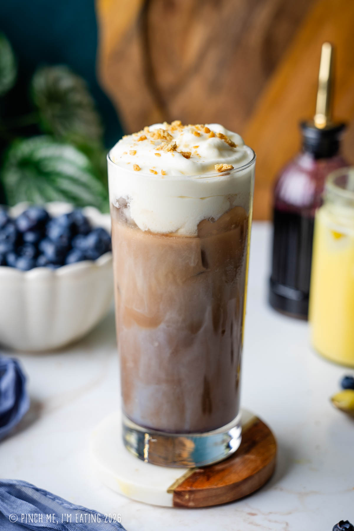 An iced blueberry latte topped with lemon curd cold foam and graham cracker crumbs, served in a tall glass.