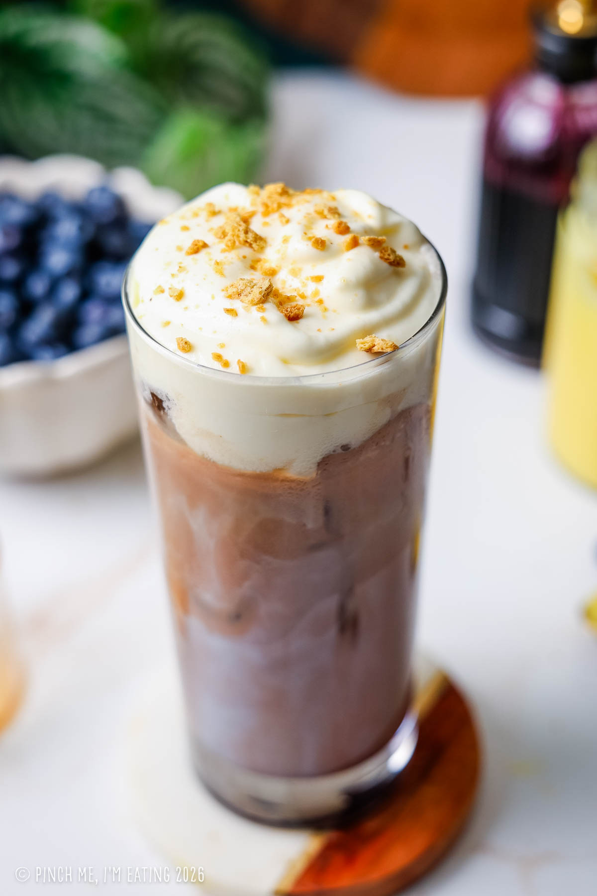 Close-up of an iced blueberry latte showing the texture of lemon curd cold foam and crushed graham crackers on top.